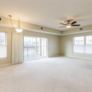 Spacious living room with carpet flooring, ceiling fan, and large windows.