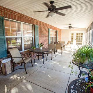 A cozy patio with outdoor furniture, ceiling fans, and potted plants against a brick wall.