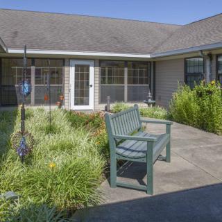 A tranquil garden patio featuring a bench surrounded by lush plants in front of a house.