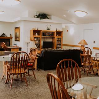 A cozy living area featuring wooden chairs, a dining table, bookshelves, and a fireplace.