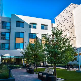 A modern courtyard with benches and trees surrounded by a multi-story building.
