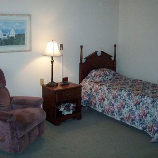 A simple bedroom with a single bed, nightstand, and armchair.