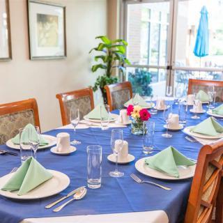 A dining table elegantly set with a blue tablecloth, green folded napkins, floral centerpiece, and neatly arranged cutlery.