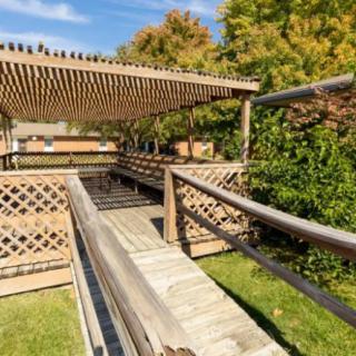 A wooden pergola with a ramp in a garden setting on a sunny day.