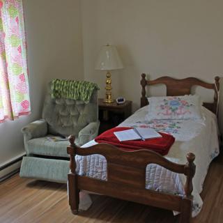 A cozy bedroom with a single bed, upholstered chair, and a lamp on a side table.