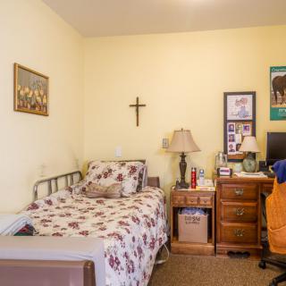 A cozy bedroom with a single bed and wooden furniture, decorated with a cross and wall art.