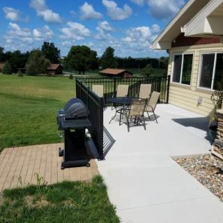 A sunny patio with outdoor seating and a grill, overlooking a spacious backyard.