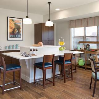 A modern kitchen featuring an island counter with bar stools, pendant lighting, and wood flooring.
