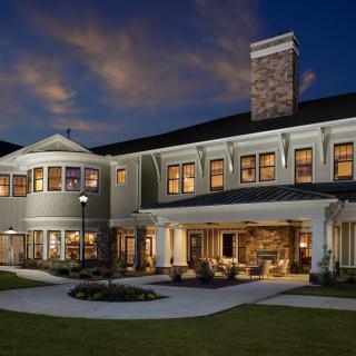 A large, two-story house illuminated at night with a spacious yard and darkening sky.