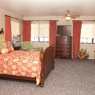 A cozy bedroom with floral bedding, multiple windows, and a dresser topped with a television.