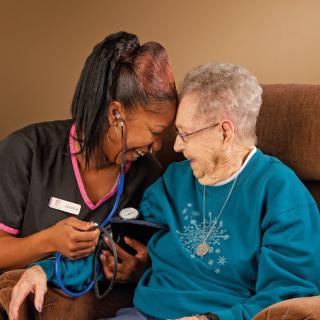 A nurse and an elderly woman share a warm moment with smiles.