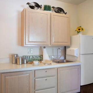 A compact kitchen area featuring wooden cabinets, a refrigerator, and countertop storage containers.