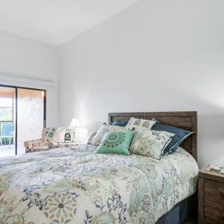 A cozy bedroom with a plush bed and decorative pillows, featuring a floral quilt and a well-lit atmosphere.