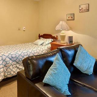 A cozy bedroom with a bed, a small couch with blue pillows, and a lamp on a bedside table.