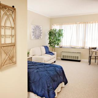 A cozy bedroom with a blue blanket on the bed, decorative elements, and ample natural light.