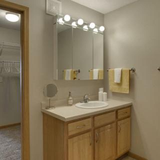 A well-lit bathroom with a wooden vanity and mirror, featuring neatly arranged towels.