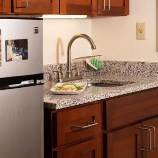 A modern kitchen with a stainless steel refrigerator, granite countertop, and wooden cabinets.