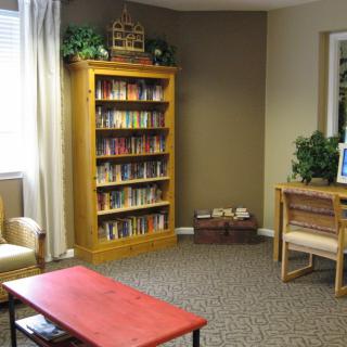 A cozy reading room featuring a wooden bookshelf filled with books, a red table, and comfortable chairs.