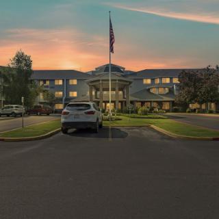 A building with a flag in front, seen at sunset with a car parked in the driveway.