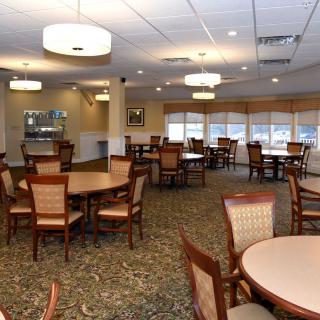 An empty restaurant dining area with multiple tables and chairs, elegantly lit by ceiling lights.