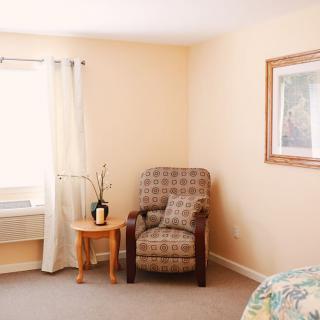 A cozy living room corner with a patterned chair, small wooden table, and window curtains.