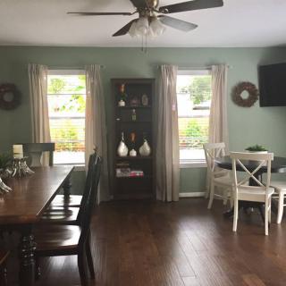 A cozy dining room with wooden floors, a large table, and a cabinet between two windows.