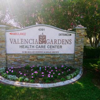 Entrance sign of Valencia Gardens Health Care Center, surrounded by a landscaped area with flowers.