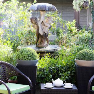 A serene garden scene featuring a charming fountain and inviting outdoor seating, perfect for enjoying tea in nature.