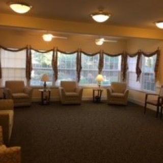 A cozy living room with several chairs, lamps, and large windows adorned with curtains.