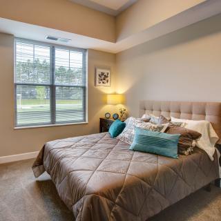 A cozy bedroom with a neatly made bed, soft pillows, and a large window letting in natural light.