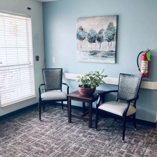 A cozy corner with two chairs and a table adorned with a plant, beneath a painting on a light blue wall.