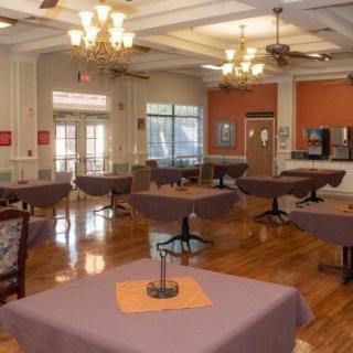 A spacious dining area featuring neatly arranged tables with purple tablecloths, elegant chandeliers, and wooden flooring.