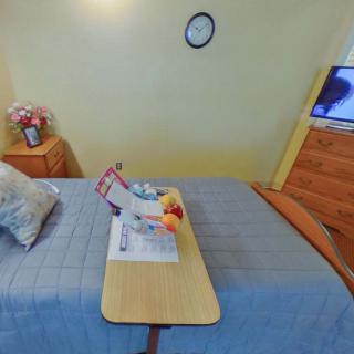 A cozy bedroom with a neatly made bed, a wall-mounted TV, and flowers on the nightstand.
