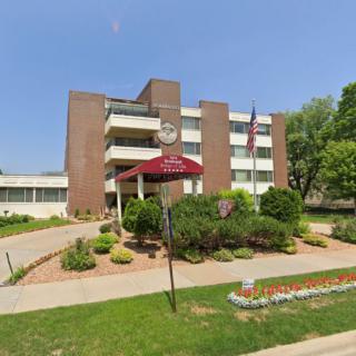 A multi-story apartment building with a landscaped entrance and a visible United States flag.