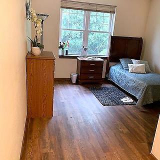 A cozy bedroom with a single bed and wooden flooring, featuring a window and neatly arranged furniture.