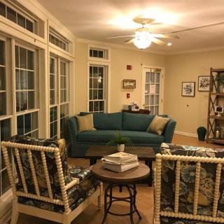 Cozy living room with a teal sofa and patterned chairs, surrounded by large windows.