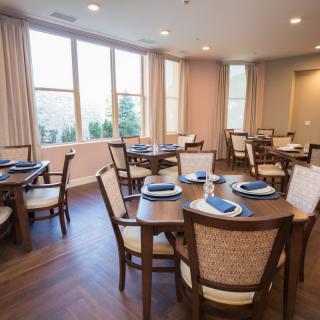 A cozy dining area with neatly arranged tables and chairs, illuminated by natural light coming through the windows.