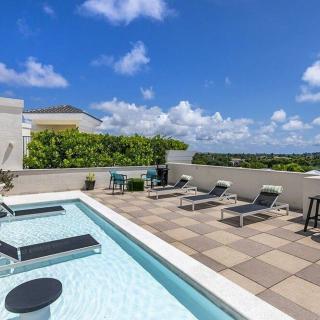 A rooftop pool area with lounge chairs under a bright blue sky.