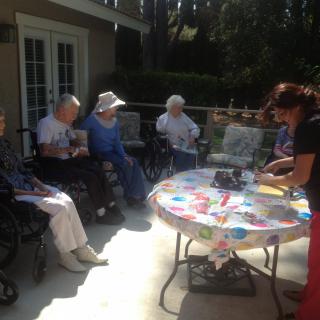 A group of elderly people sitting outdoors, enjoying a sunny day together around a table.