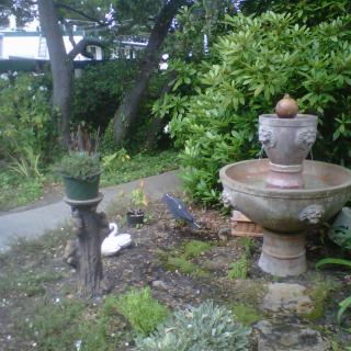 A serene garden scene featuring a decorative fountain, lush greenery, and statues.