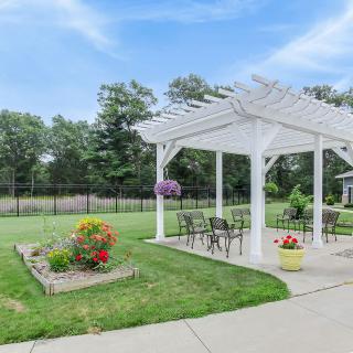 A scenic outdoor area with a white pergola, garden flowers, and patio furniture.