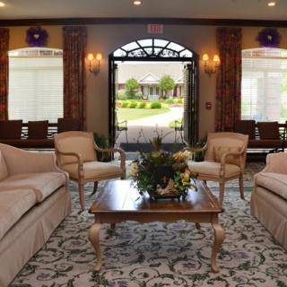 A well-decorated living room with comfortable sofas and chairs arranged around a coffee table, featuring an elegant carpet and an open archway leading to an outdoor view.