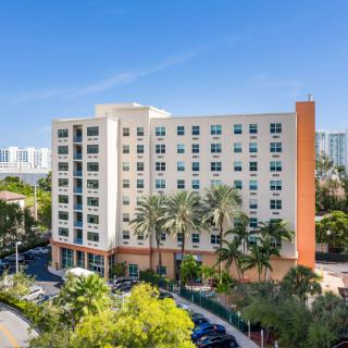 A modern residential apartment building surrounded by palm trees in an urban setting.