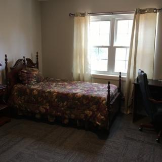 A simple bedroom with a single bed, a desk, and a window with curtains.