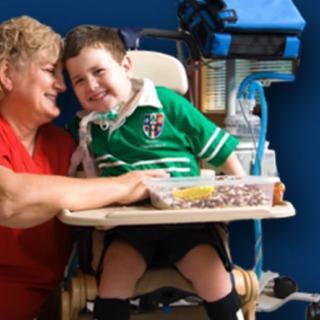 A woman lovingly embraces a smiling child sitting in a wheelchair, symbolizing care and support.