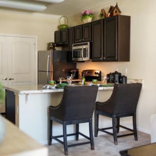 A modern kitchen with dark cabinets, a stainless steel fridge, and bar stools at the counter.