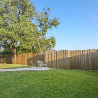 A serene backyard with a wooden fence, lush grass, and a patio set under a tree.