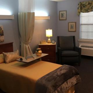 A cozy bedroom with soft lighting, featuring a bed, armchair, and decorative accents.