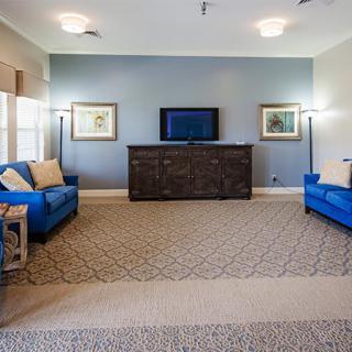 A modern living room with blue sofas, a television on a dark dresser, and decorative lamps and artwork.