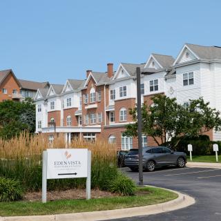 A residential building with a sign in front, surrounded by trees and grass.